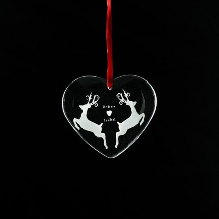 Heart-shaped crystal Christmas ornament with an engraved reindeer design, hanging from a red ribbon.