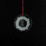 Personalized round crystal Christmas ornament with an engraved family name inside a wreath design.