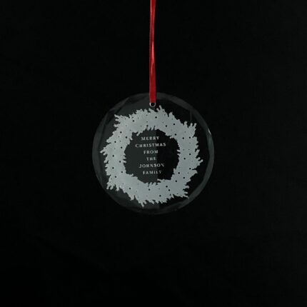 Personalized round crystal Christmas ornament with an engraved family name inside a wreath design.