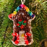 Colorful gingerbread house Christmas ornament with candy canes, a wreath, and rainbow rhinestone gumdrops, made from brown and colored rubber bands.