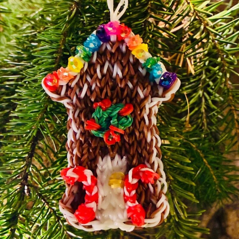 Colorful gingerbread house Christmas ornament with candy canes, a wreath, and rainbow rhinestone gumdrops, made from brown and colored rubber bands.