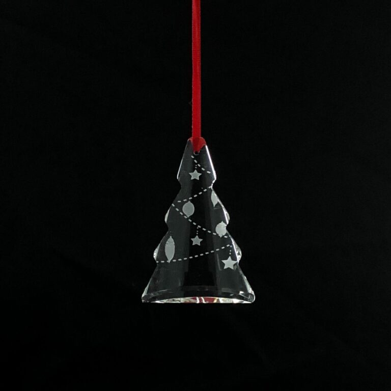 Christmas tree-shaped crystal ornament hanging from a red ribbon on a pine tree.