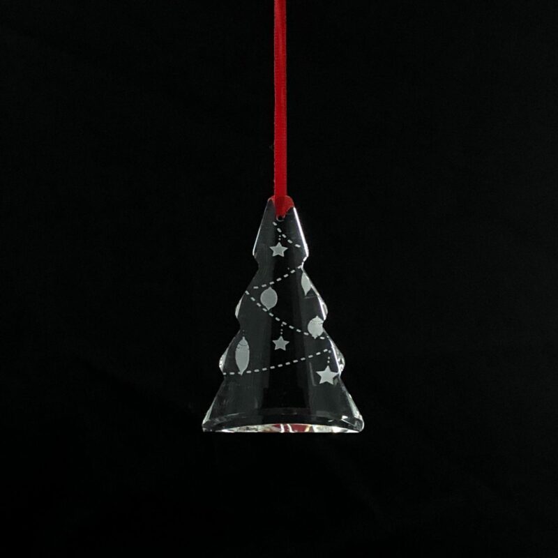 Christmas tree-shaped crystal ornament hanging from a red ribbon on a pine tree.