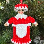 Handmade Mrs. Claus Christmas ornament in an apron, made from red, white, and gray rubber bands with sparkling rhinestone eyes.